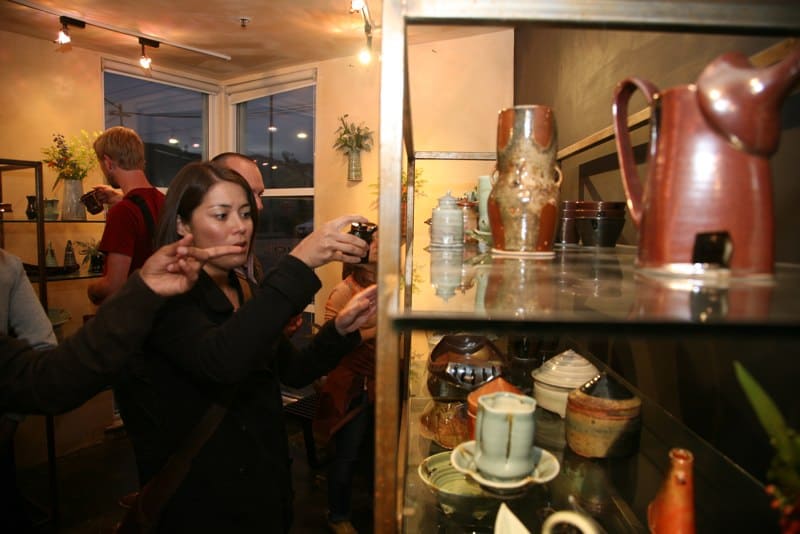 Woman browsing and taking photos of Japanese pottery in a shop.