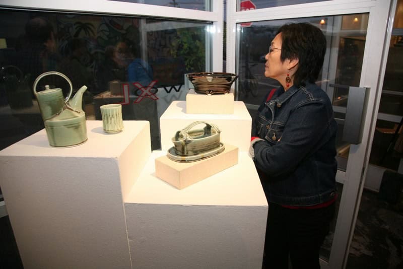 Woman viewing handcrafted ceramic ware at an art exhibition.